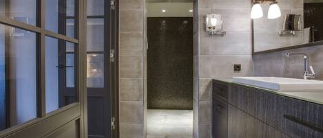 Une salle de bain moderne avec un grand miroir, un lavabo et un espace douche.