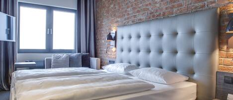 Quarto de hotel moderno com uma cama grande, parede de tijolos e televisão.