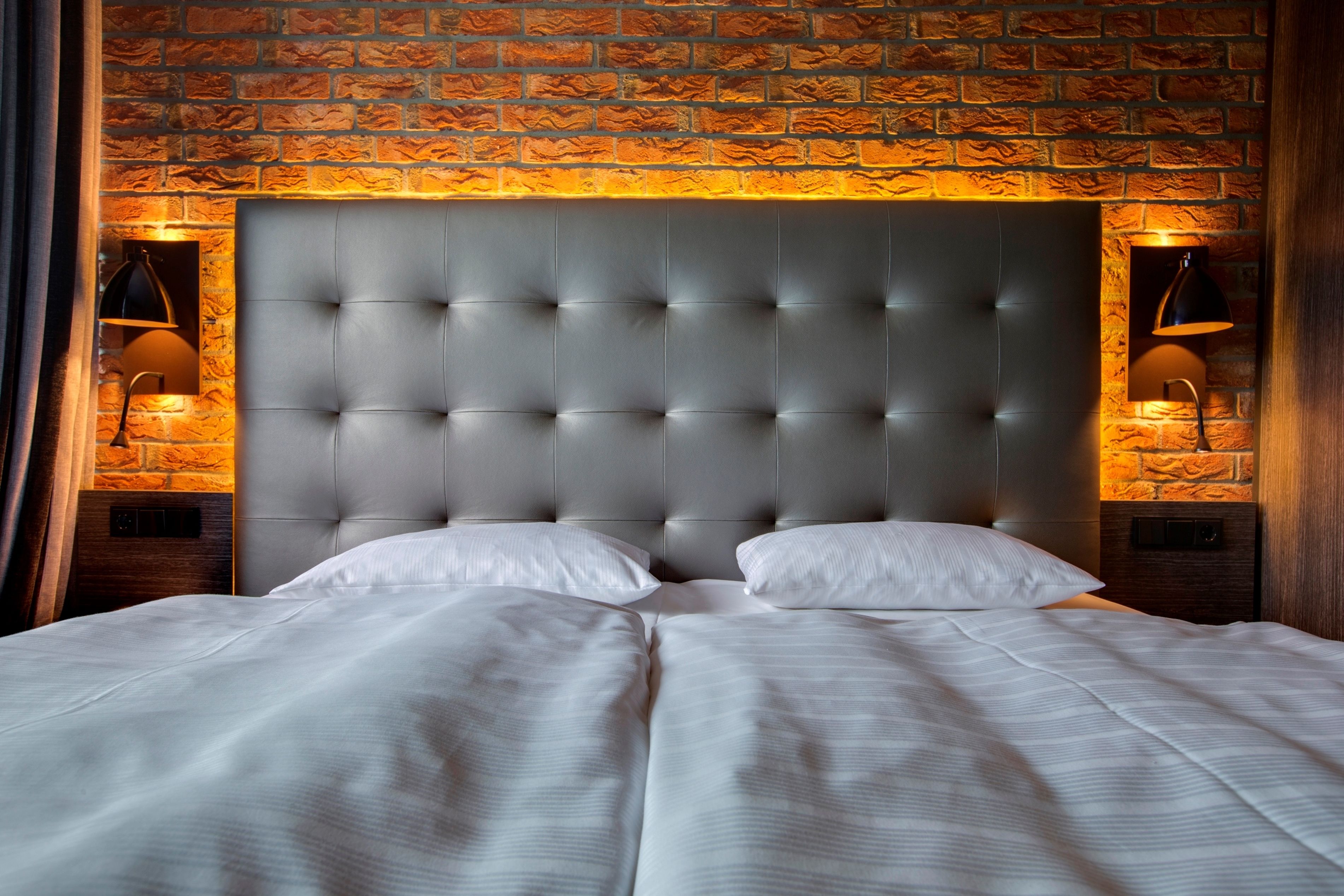 A bed with a tufted headboard, two bedside lamps, and a brick-patterned wall.