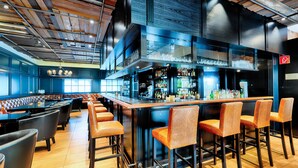Uma área de bar com bancos altos, balcão e um espaço de estar com mesas e cadeiras.
