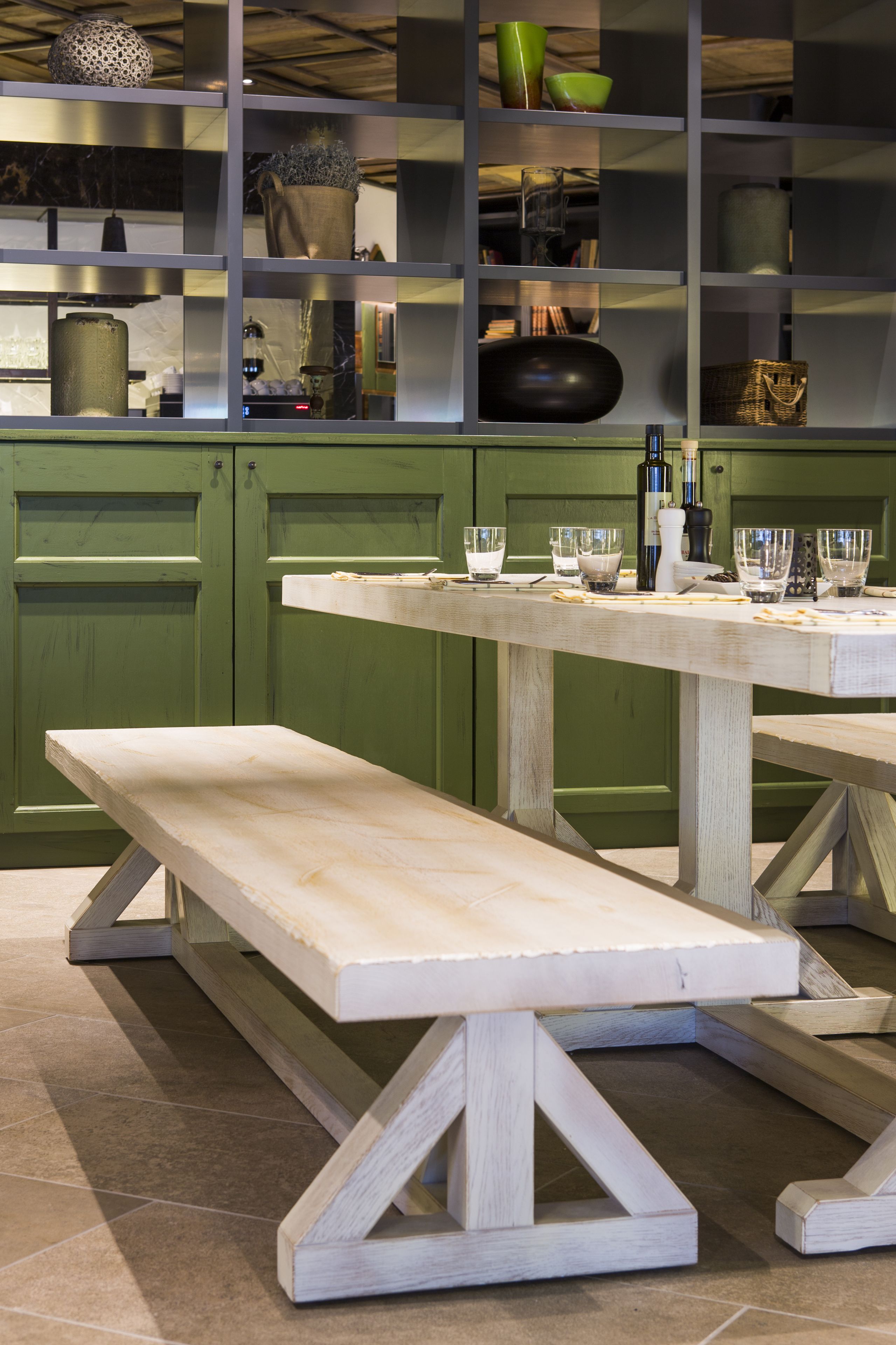 Un banco y una mesa de madera en una cocina con armarios verdes y varios utensilios.