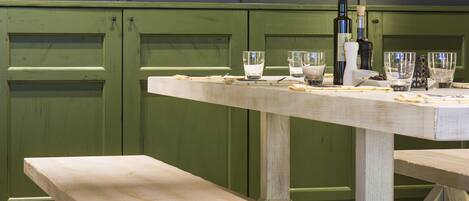 Un banco y una mesa de madera en una cocina con armarios verdes y varios utensilios.