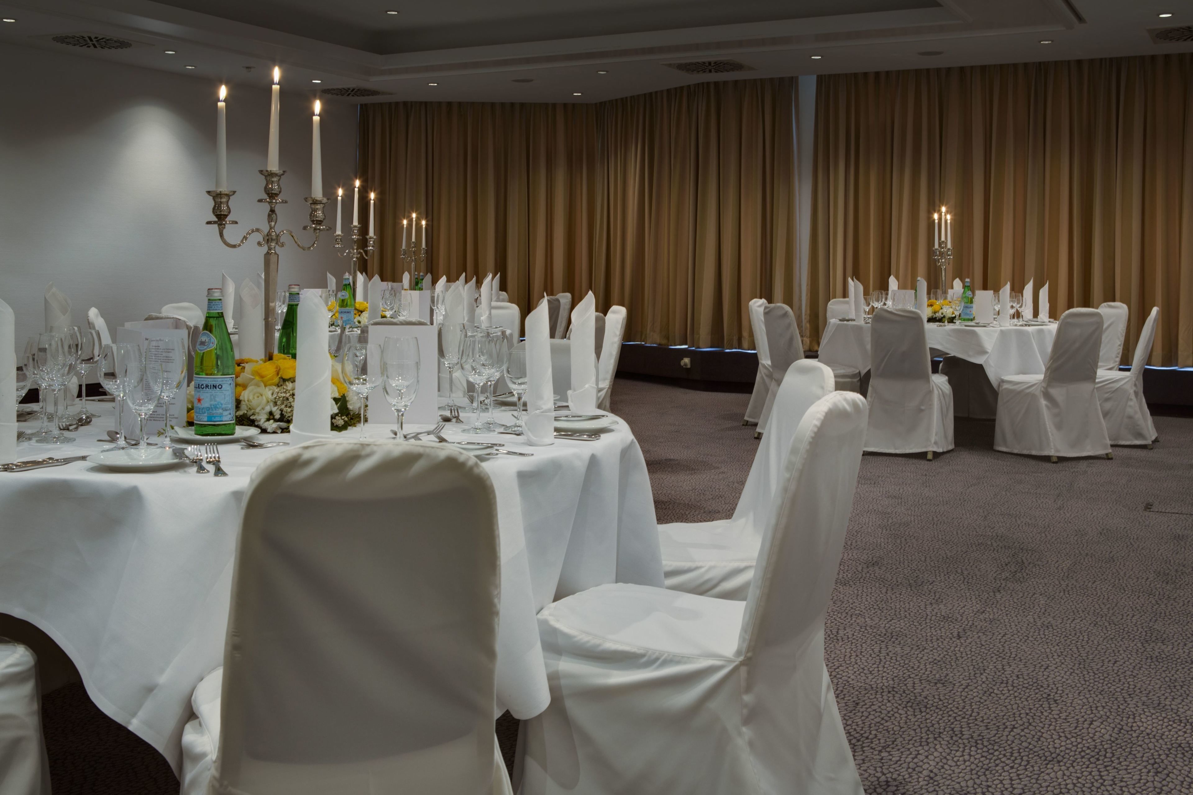 A banquet hall with round tables set for dining, white chairs, and candelabras.