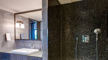 Un baño moderno con un espejo grande, un lavamanos y una ducha con un muro de mosaicos.