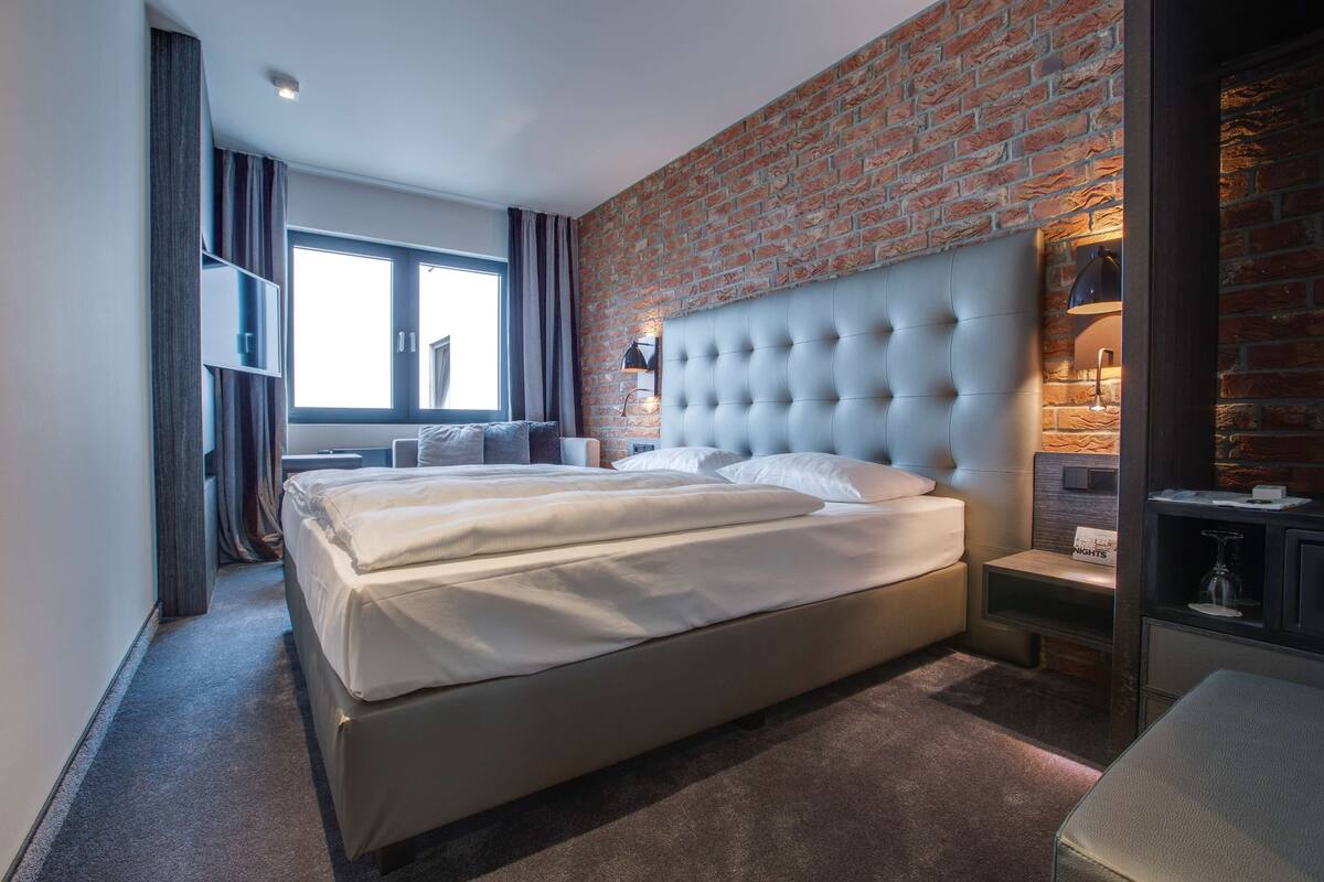 Una habitación de hotel moderna con una cama grande, una pared de ladrillo y una ventana con cortinas.
