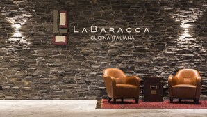 A stone wall with the text "LABARACCA CUCINA ITALIANA" and two leather armchairs with a small table in front.