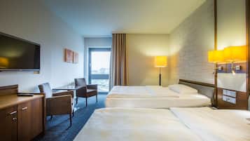 A hotel room with two beds, a desk with a chair, a TV, and a window with curtains.