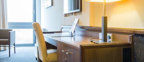 A hotel room with a desk, chair, television, and a large window.