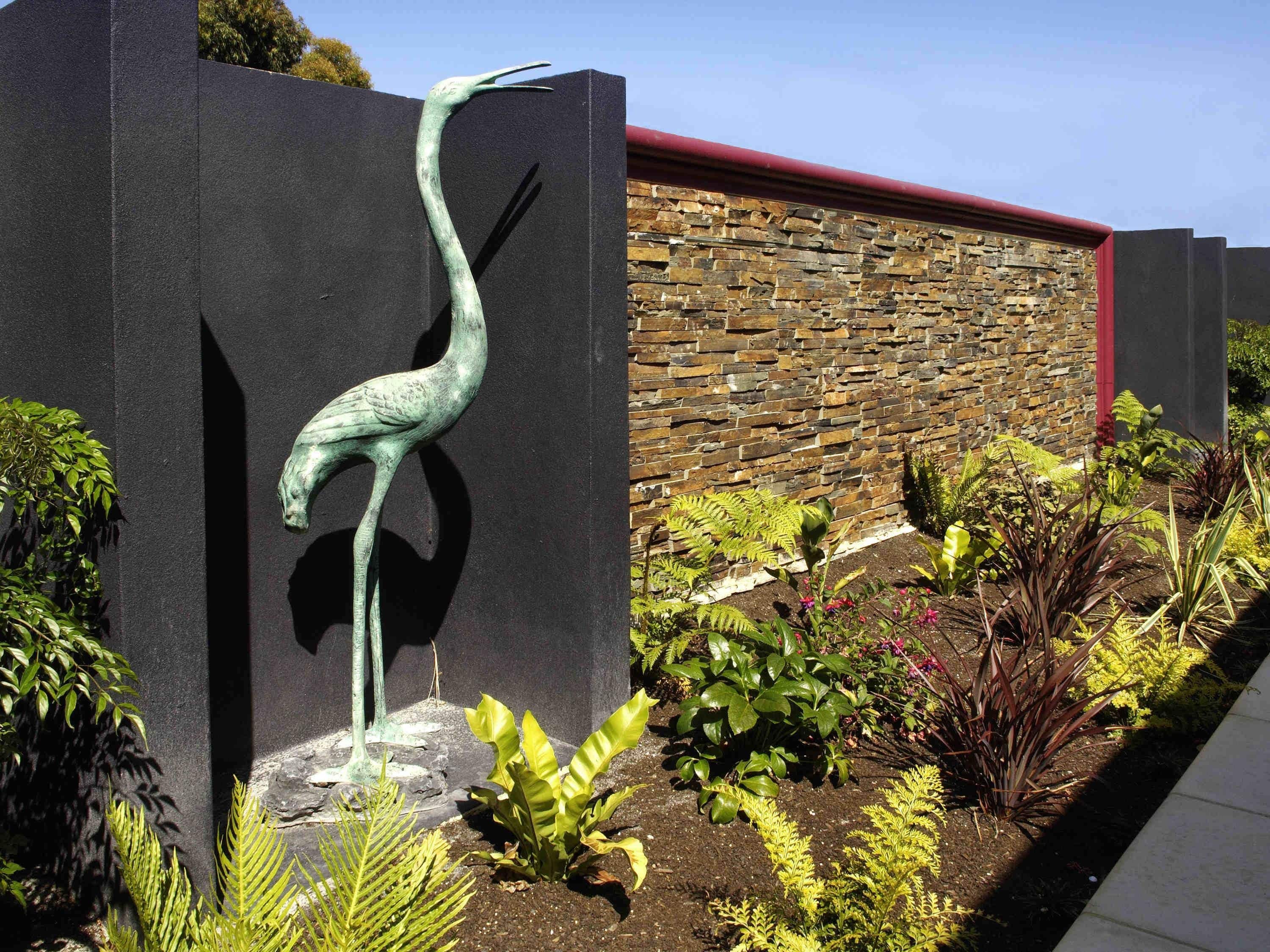A bronze sculpture of a bird, possibly a crane, mounted on a black wall.