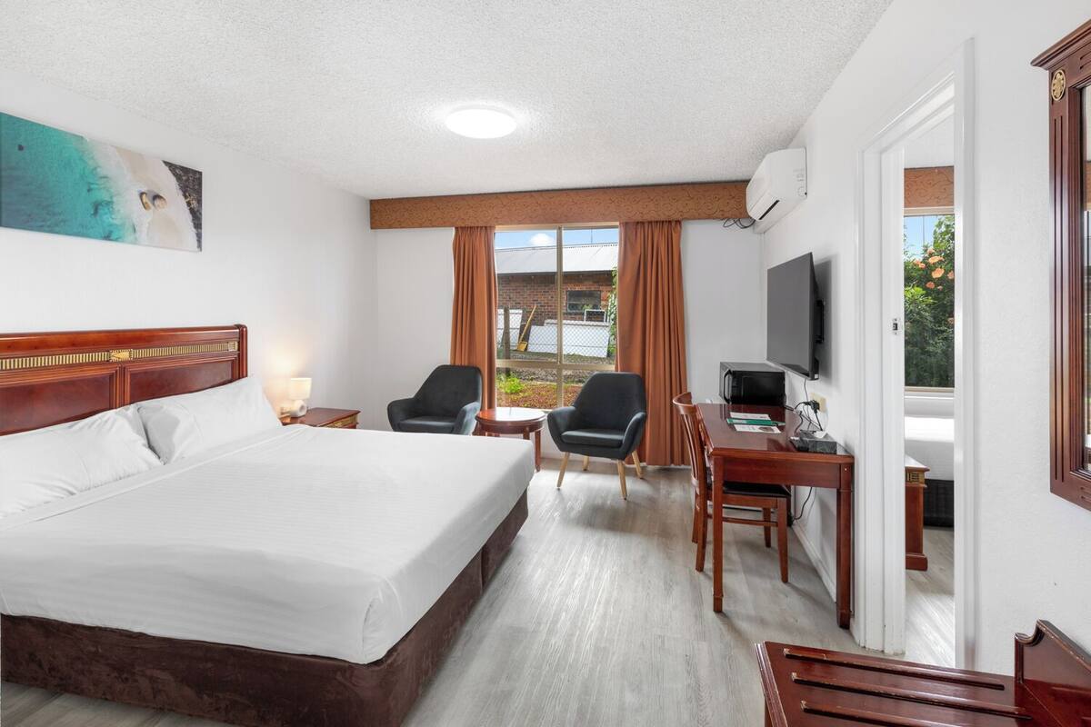 Habitación de hotel con una cama grande, dos sillones, un escritorio con televisor y una ventana con cortinas.