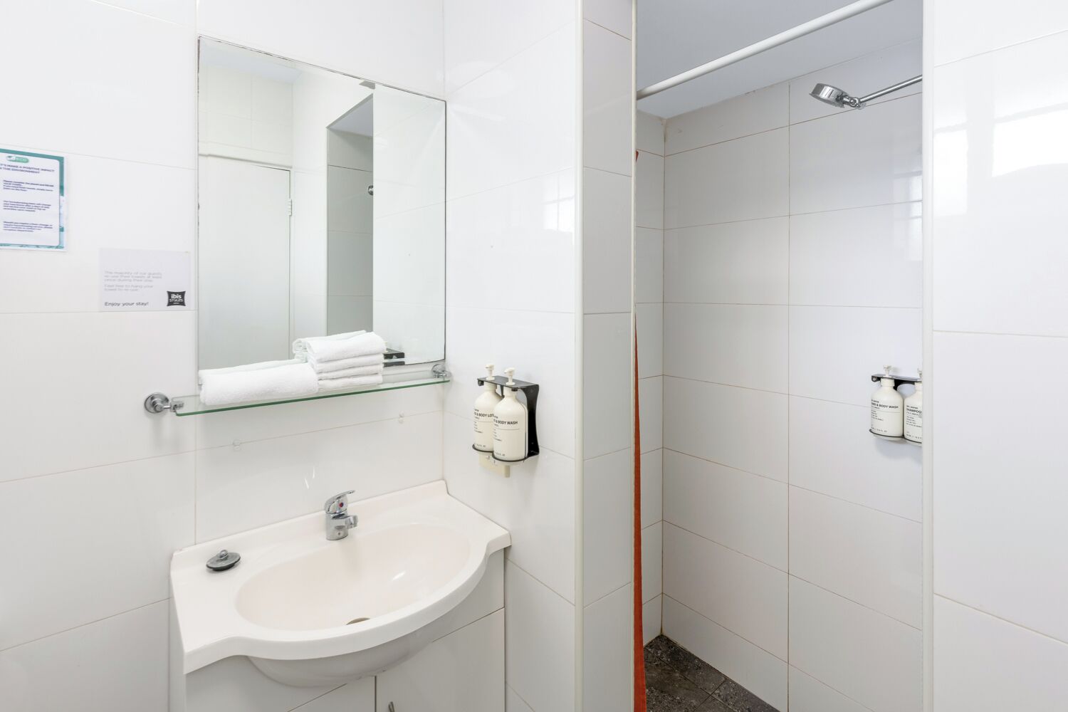 Un baño moderno con un lavabo blanco, una repisa de vidrio con toallas, un espejo y dos cabezales de ducha.