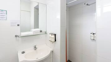Un baño moderno con un lavabo blanco, una repisa de vidrio con toallas, un espejo y dos cabezales de ducha.