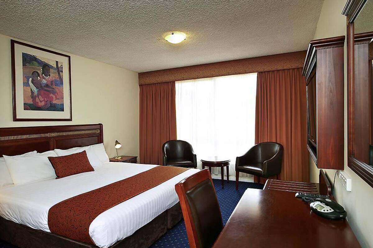 Habitación de hotel con una cama grande, dos sillas, una mesita y un escritorio con teléfono.