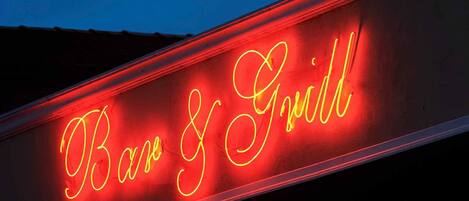 Un letrero de neón con las palabras 'Bar & Grill' escritas en letra cursiva.