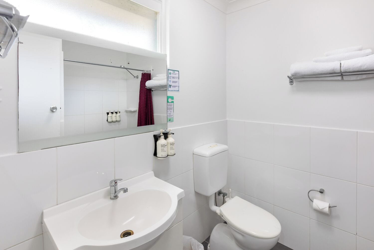 A modern bathroom with a white sink, toilet, and shower area. There is a mirror above the sink and a towel rack on the wall.