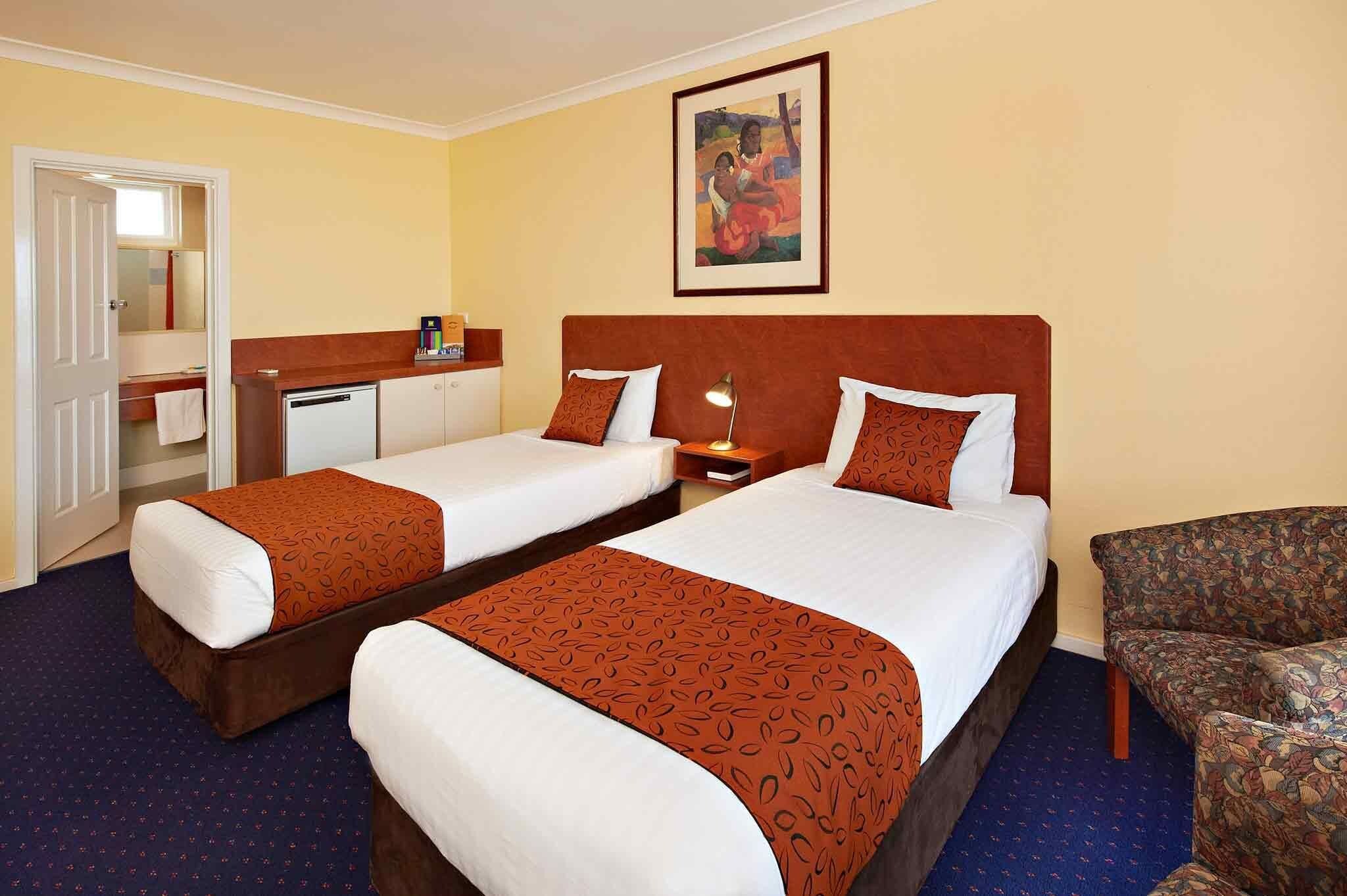 Een hotelkamer met twee bedden, een zithoek, een badkamer en een schilderij aan de muur.