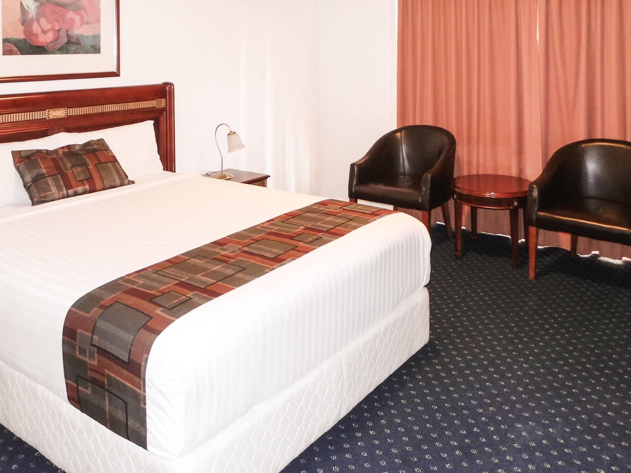 A hotel room with a large bed, two chairs, a small table, and a lamp.