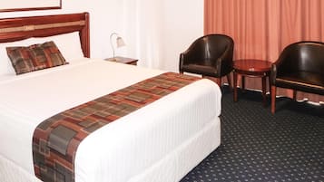 A hotel room with a large bed, two chairs, a small table, and a lamp.