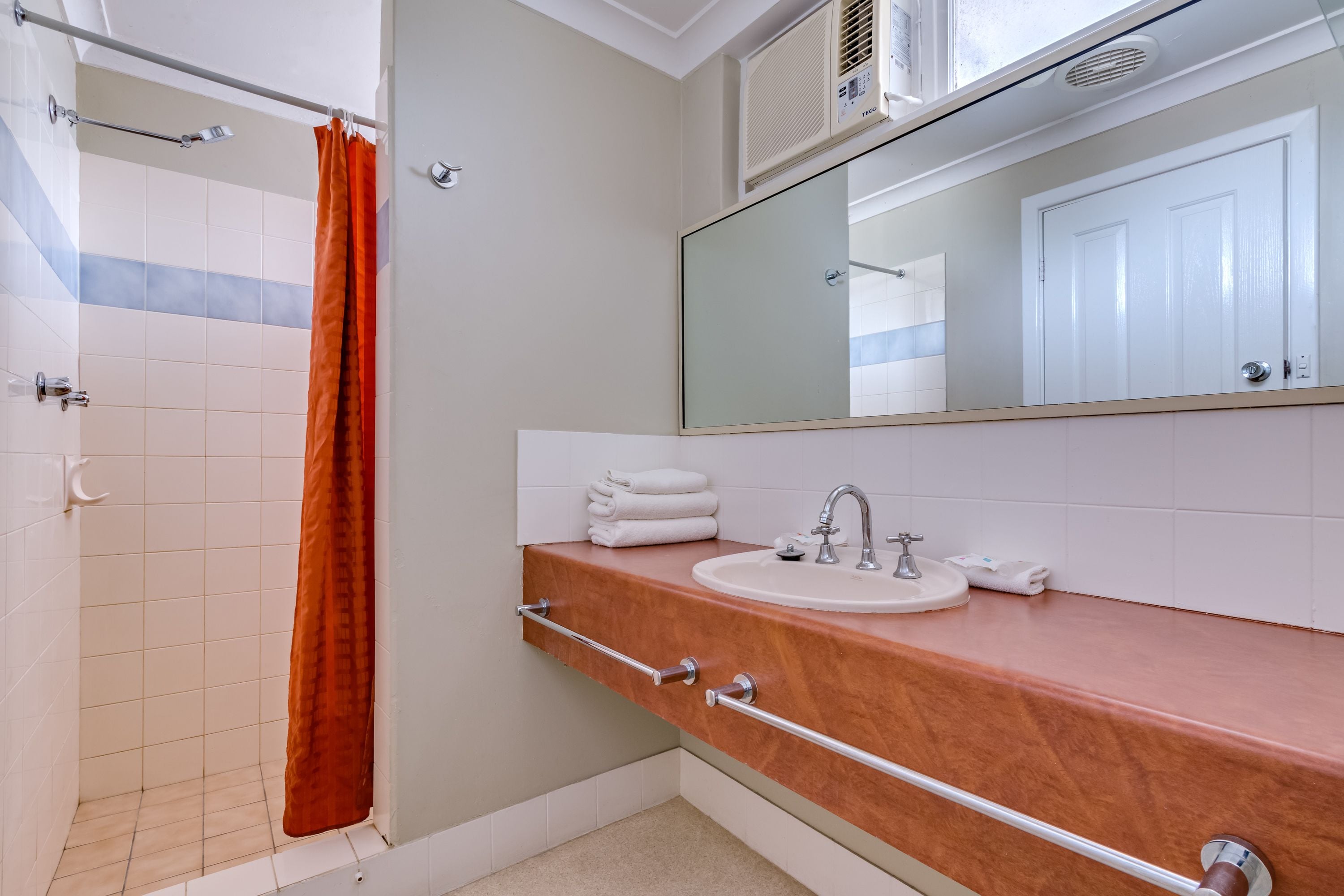 A bathroom with a shower, a sink with a mirror, and a towel rack.
