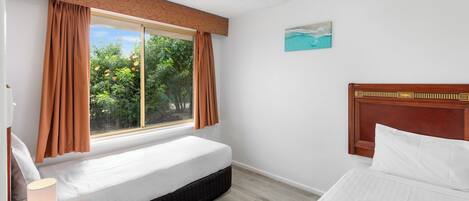 Un dormitorio con cama, mesita de noche con lámpara, ventana con cortinas y un cuadro en la pared.