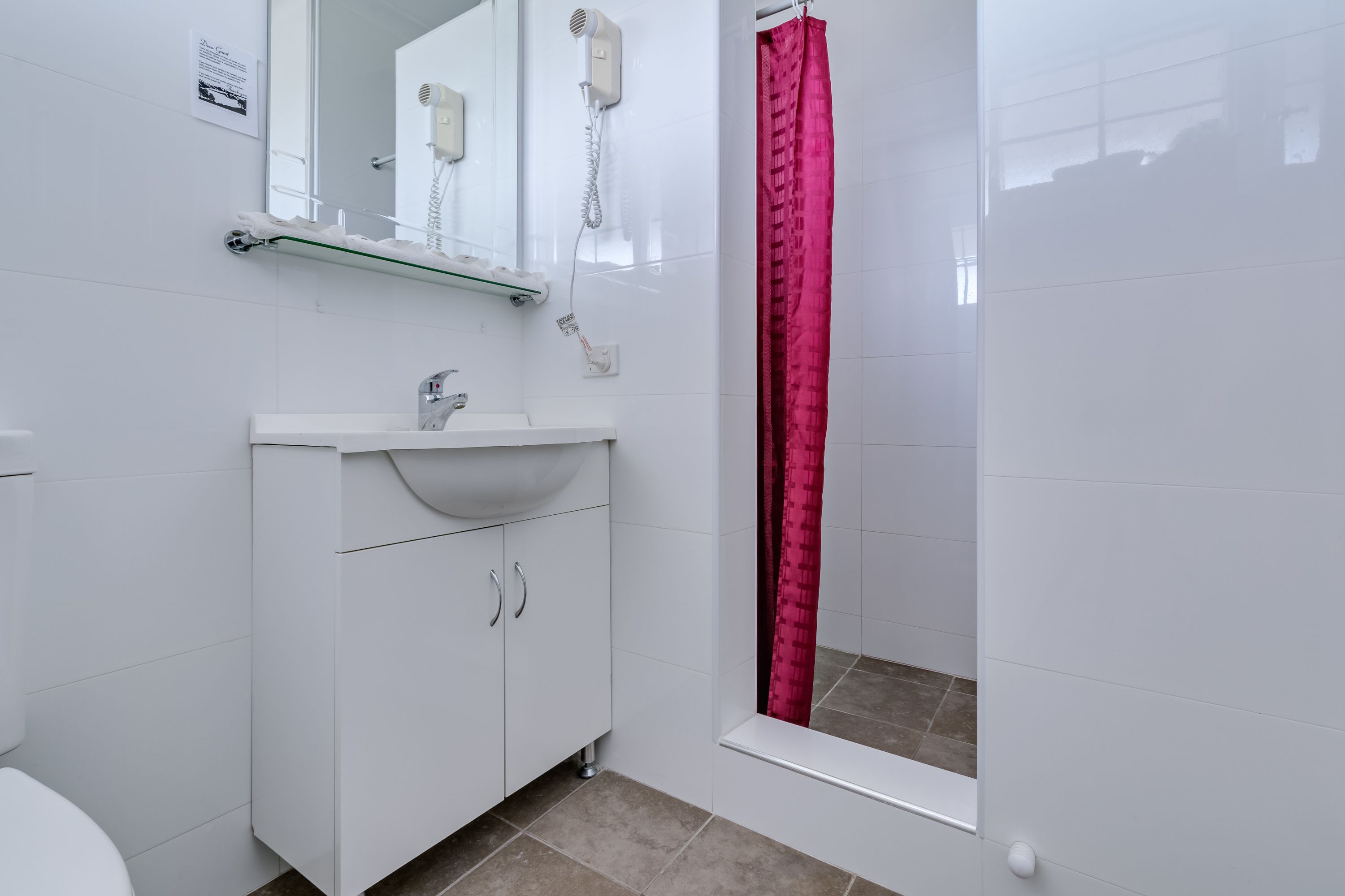 Un baño con un lavabo blanco, un espejo, un secador de pelo y una ducha con cortina roja.