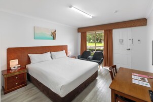 Habitación de hotel con una cama grande, un escritorio, dos sillas, un televisor y una ventana con cortinas.