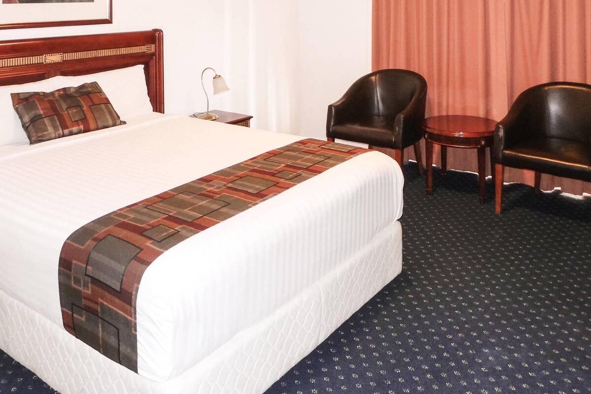 Una habitación de hotel con una cama grande, dos sillas, una mesita y una lámpara.