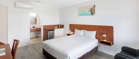 A hotel room with a large bed, a desk with a chair, a small kitchenette, and a bathroom visible through an open door.