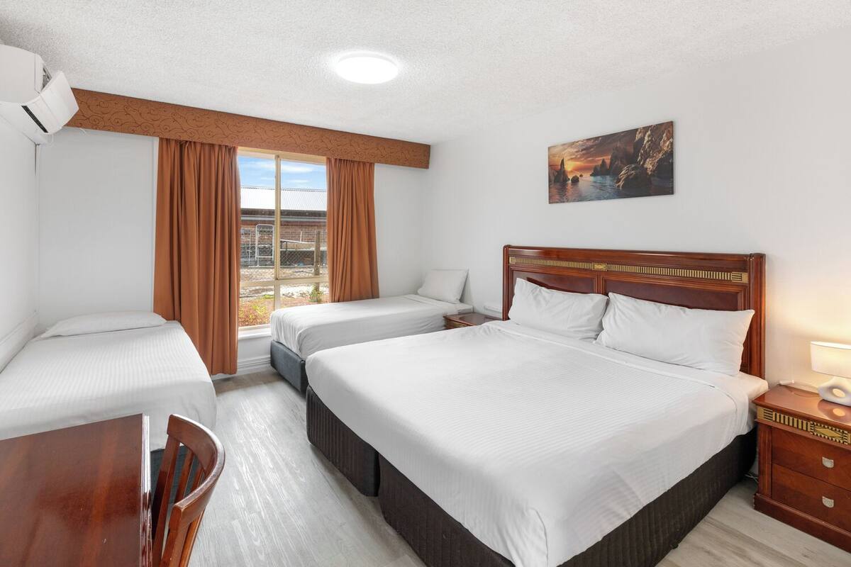 Habitación de hotel con dos camas individuales, cabecero de madera, escritorio y una silla.