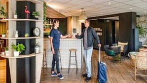 A modern hotel lobby with a bar area, wooden flooring, and a decorative flamingo sculpture. - ibis Styles Albany (Orana)