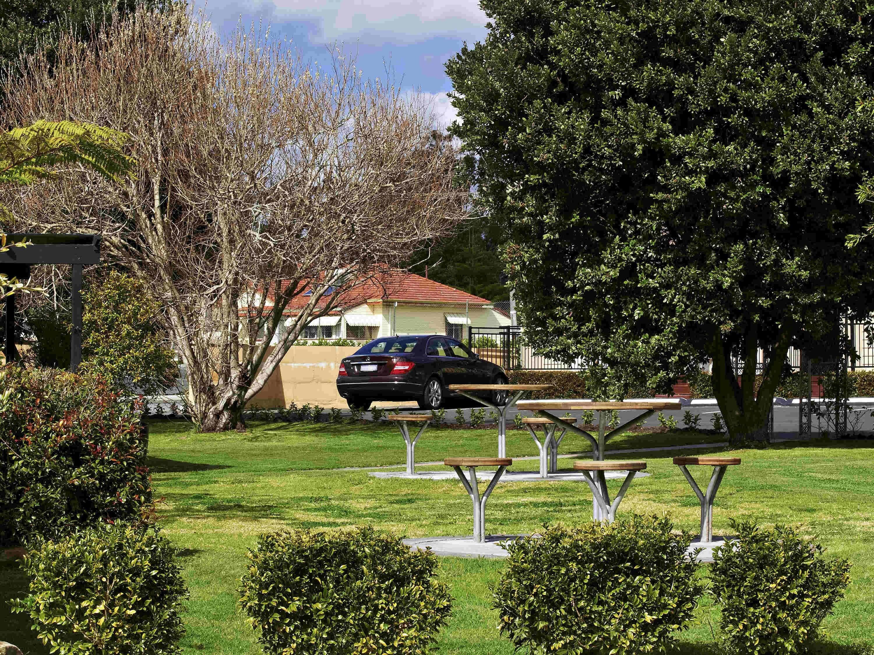 Un parque con mesas de picnic, un coche y una casa de techo rojo.