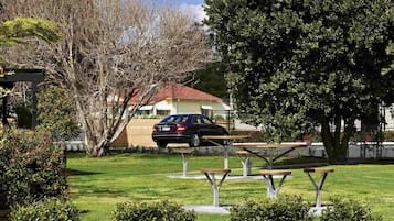 Un parque con mesas de picnic, un coche y una casa de techo rojo.