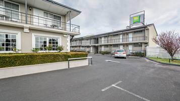 A modern hotel with a two-story structure, a parking area, and a sign for 'ibis Studios'.