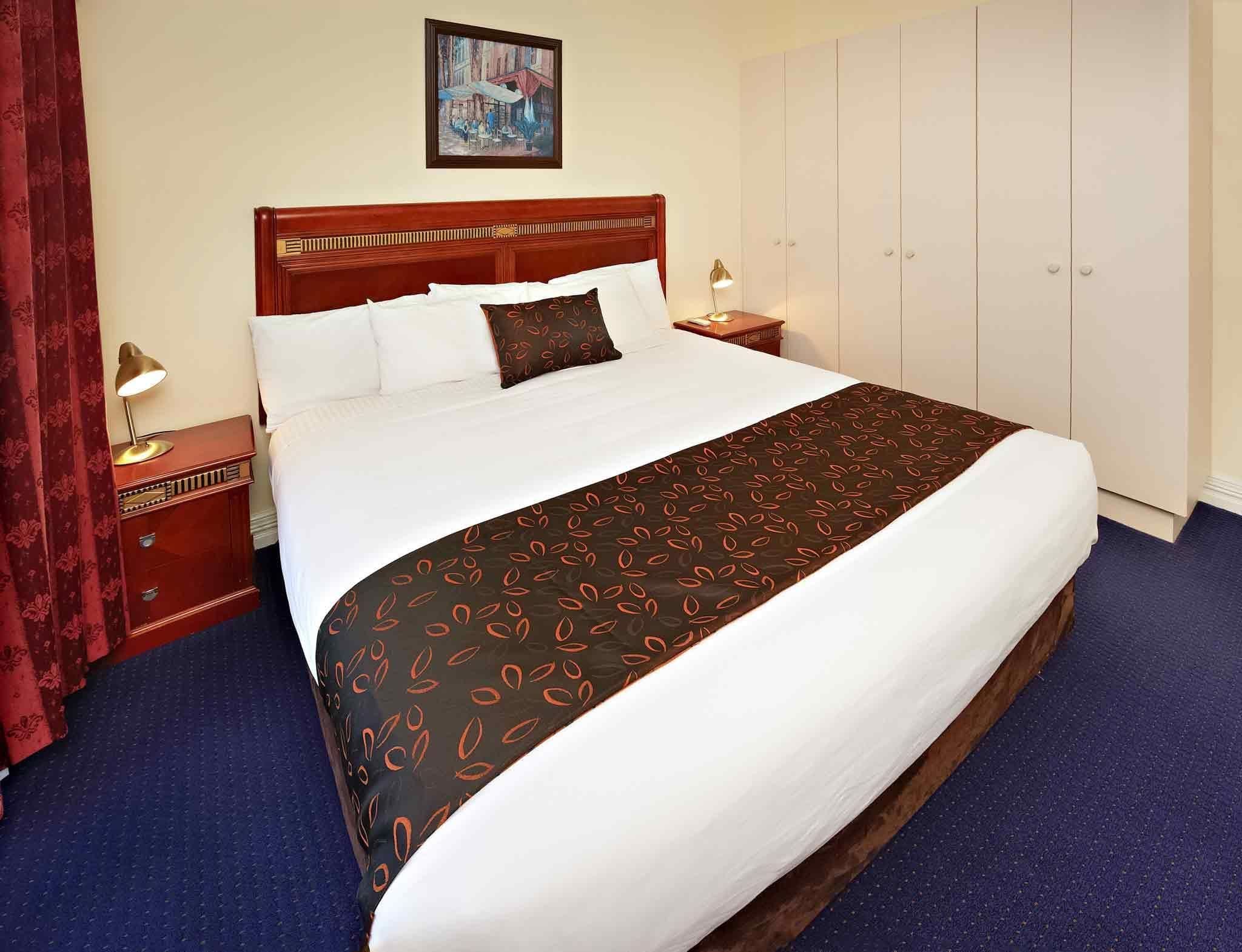 A hotel room with a large bed, a wardrobe, a nightstand, and a painting on the wall.