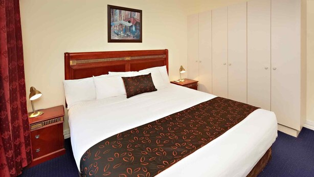 Habitación de hotel con una cama grande, un armario, una mesita de noche y un cuadro en la pared.