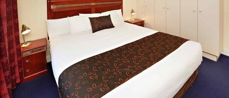 A hotel room with a large bed, a wardrobe, a nightstand, and a painting on the wall.