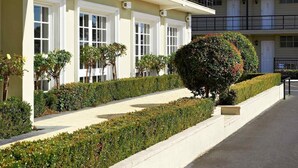 A row of two-story buildings with white-framed windows, a well-maintained hedge, and a clear sidewalk. - ibis Styles Albany (Orana)