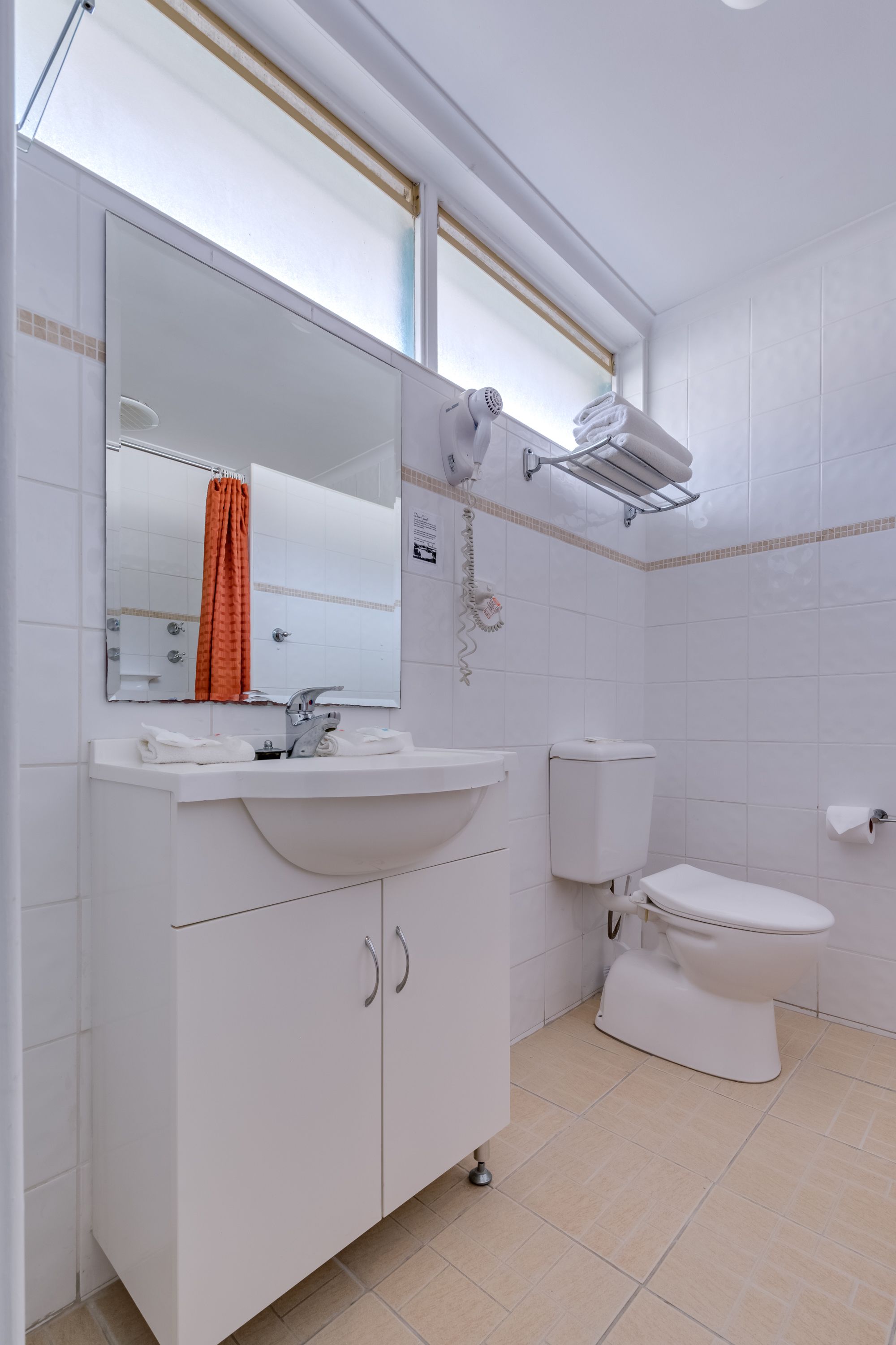 Un baño con lavamanos, espejo y retrete blancos.
