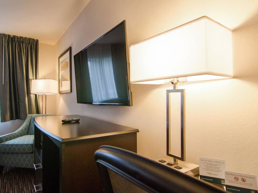 Habitación de hotel con escritorio, silla, televisor, lámpara y letrero que indica prohibido fumar.