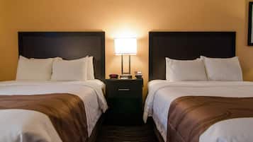 A hotel room with two beds, a nightstand with a lamp, and a wall-mounted phone.