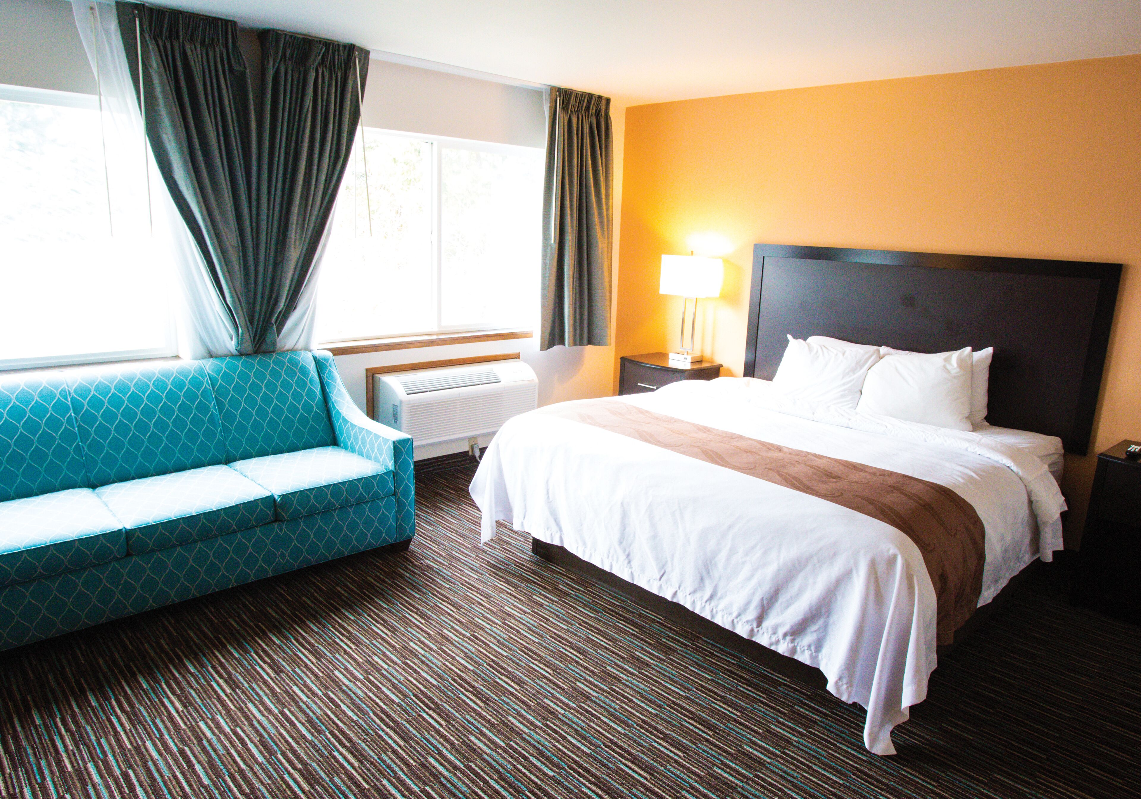 A hotel room with a bed, a sofa, a lamp, and a window with curtains.