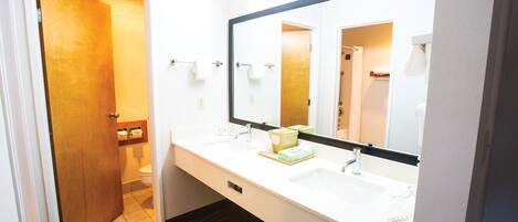Un baño de hotel con un espejo grande, dos lavamanos y una puerta de madera que da al inodoro.