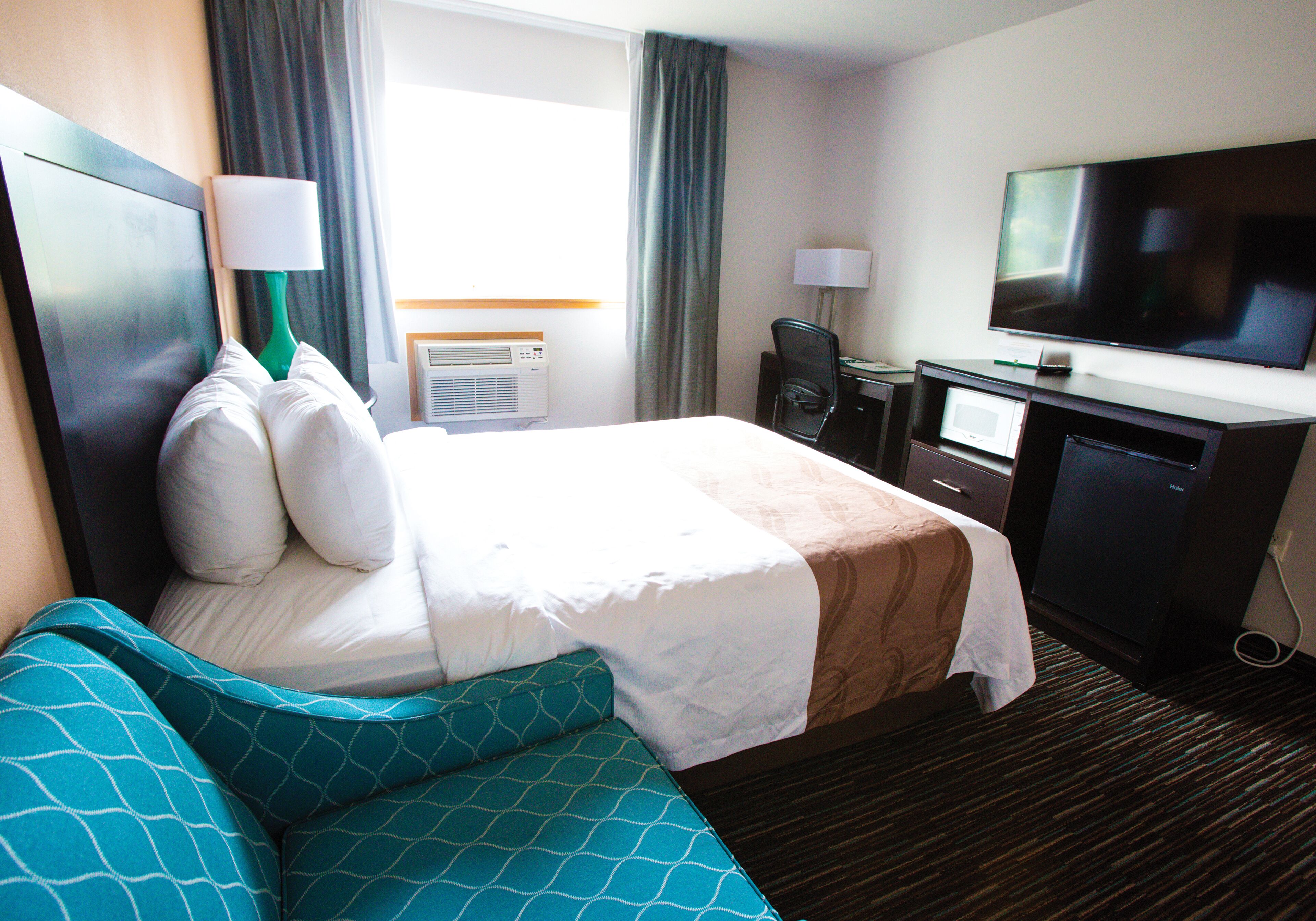 A hotel room with a bed, a desk, a television, and a window with curtains.