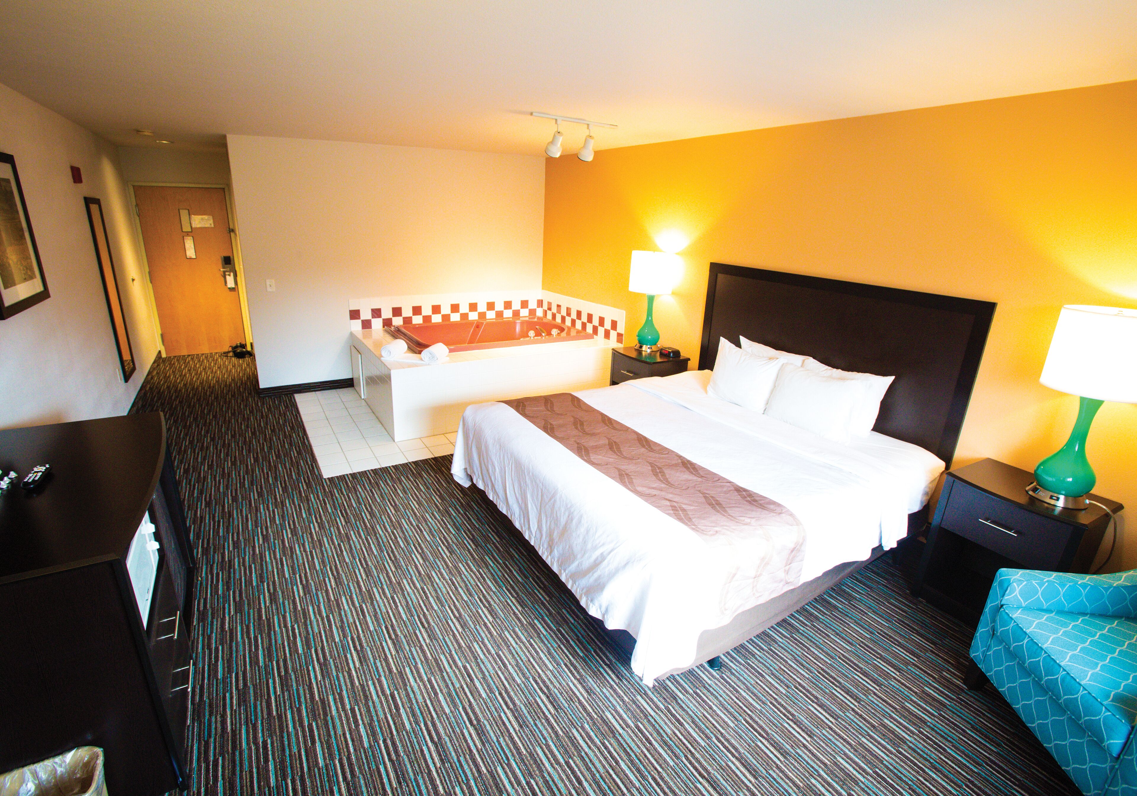 A hotel room with a bed, bedside tables, a desk, a chair, and a bathroom with a bathtub.