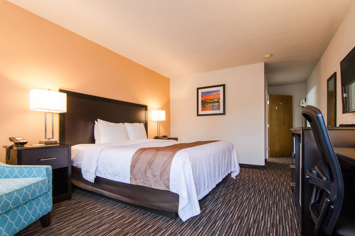 A hotel room with a large bed, two bedside lamps, a desk with a chair, and a framed picture on the wall.