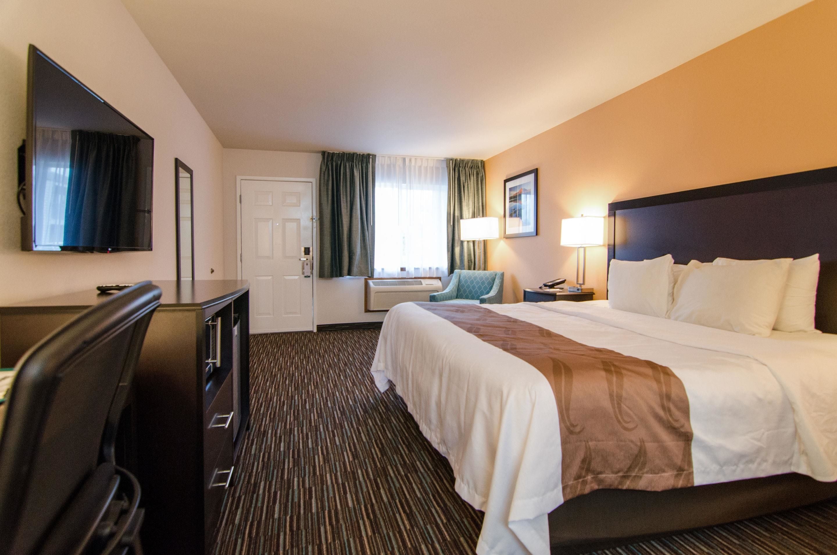 A hotel room with a bed, a desk, a chair, a TV, and a lamp.