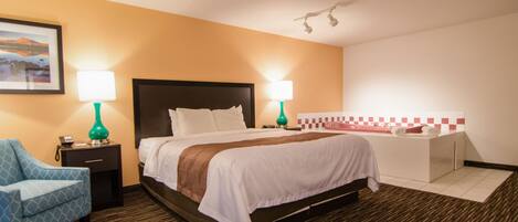 A hotel room with a bed, two bedside tables with lamps, a chair, a bathroom with a bathtub, and a wall-mounted light fixture.