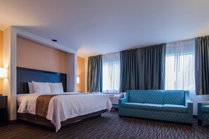 A hotel room with a bed, a sofa, a chair, a nightstand, and a window with curtains. - Cottage Grove Inn (Cottage Grove)