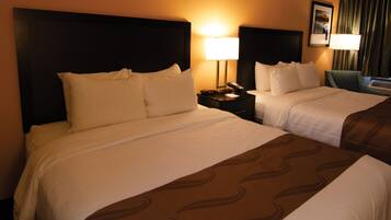 Habitación de hotel con dos camas, una mesita de noche con lámpara y una silla.