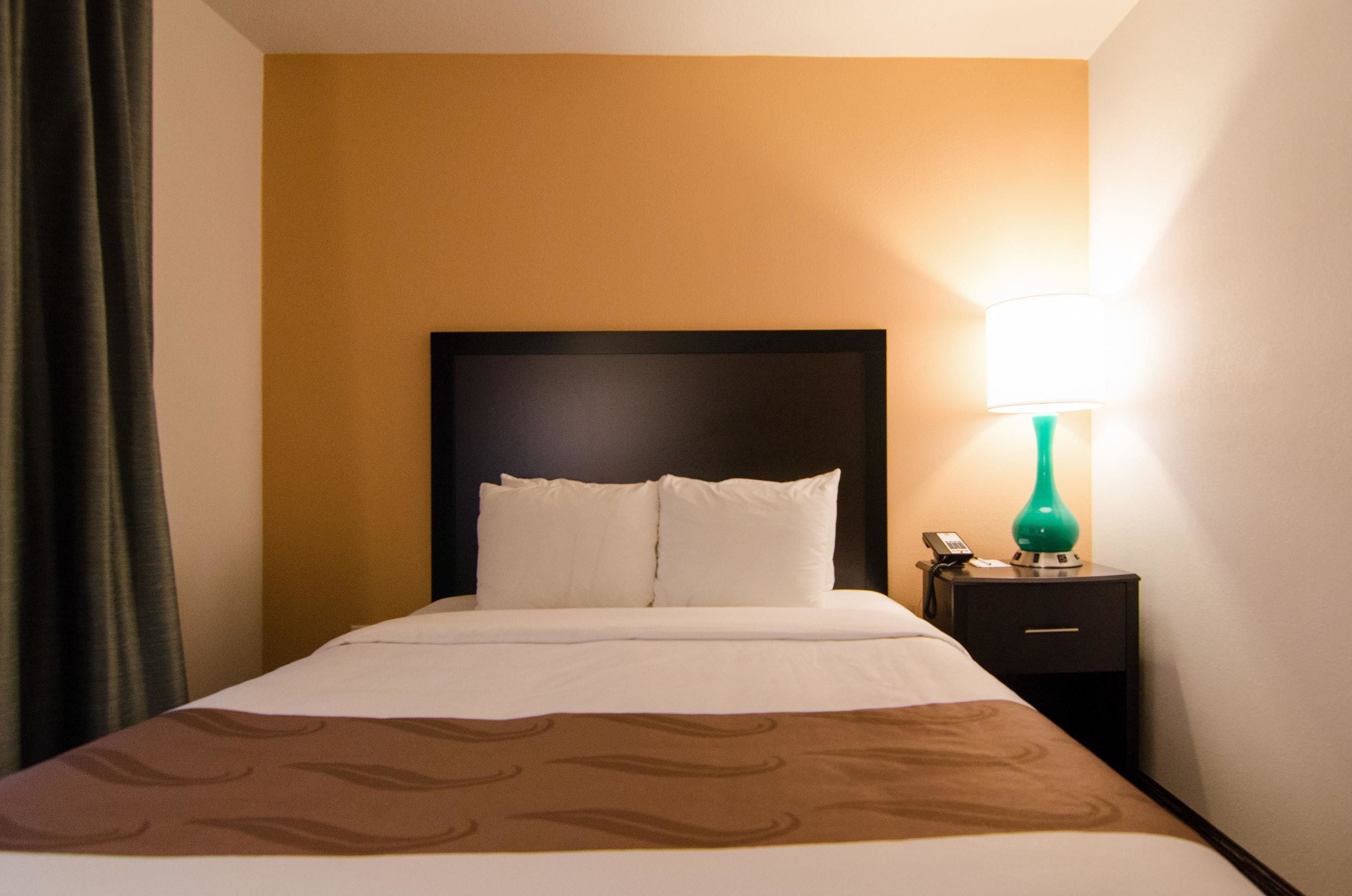 A hotel room with a bed, a nightstand, a lamp, and a curtain.